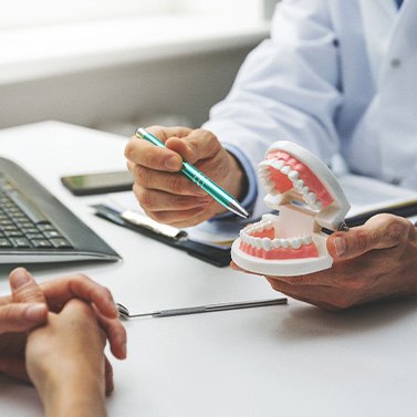 Hands of dentist and patient at desk with model teeth discussing treatment plan