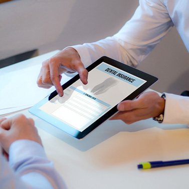 Hands of dentist and patient at desk looking at dental insurance on digital tablet