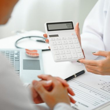 Hands of dentist holding calculator to show patient potential cost