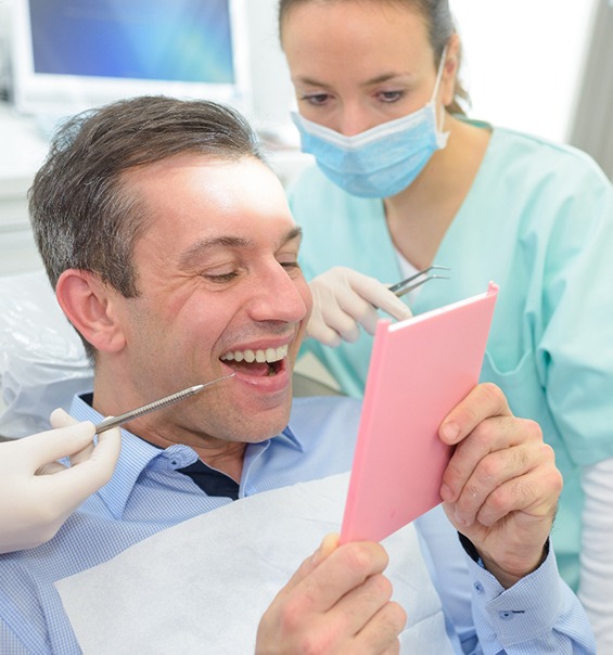 Man in dental chair smiling into mirror with dentist over his shoulder