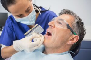 Dentist holding shade guide to man's teeth