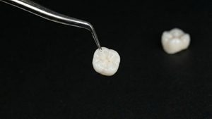 Tweezers grasping dental crown from black surface